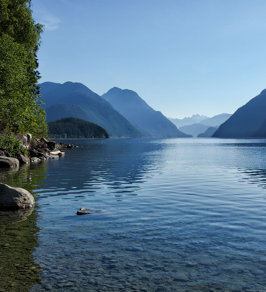 Calm waters on Alouette Lake in Maple ridge on a sunny day with a valley of mountains in the distance.